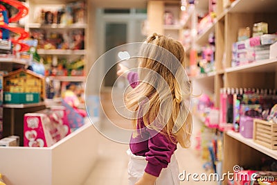 Back view of adorable little girl shopping for toys. Cute female in toy store. Happy young girl selecting toy Stock Photo