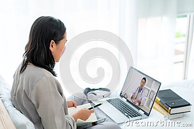 Back view of Asian woman making video call with her doctor with her feeling sick on laptop in bedroom for online healthcare Stock Photo