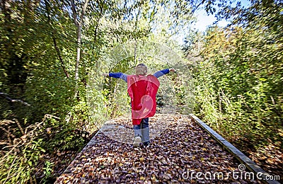 Back view of boy jumping with red cape outside Stock Photo