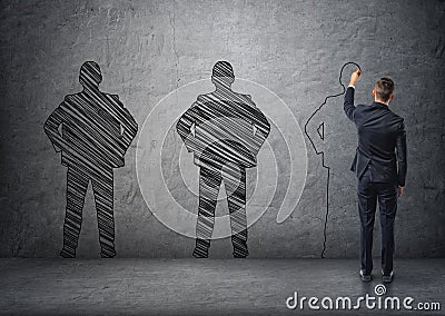 Back view of a businessman drawing dark men's silhouettes on concrete wall Stock Photo