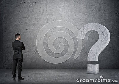 Back view of a businessman looking at big 3D concrete question mark Stock Photo