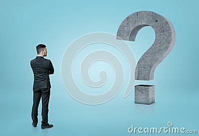 Back view of a businessman looking at big 3D concrete question mark isolated on blue background Stock Photo