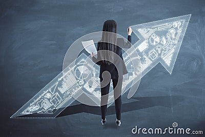 Back view of businesswoman with upward business arrow sketch drawing on chalkboard wall background. Success, finance and Stock Photo
