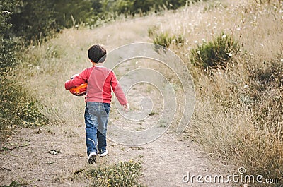 Back view of a child with a ball in his arm walking down a road Stock Photo