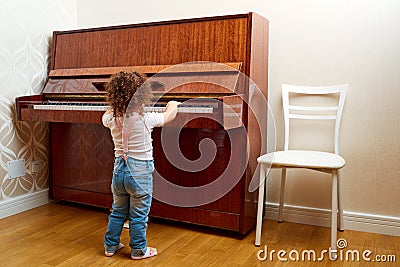 Back view. A child stands in front of the piano and plays a melody. Little pianist learning to play the piano. Baby, child Stock Photo