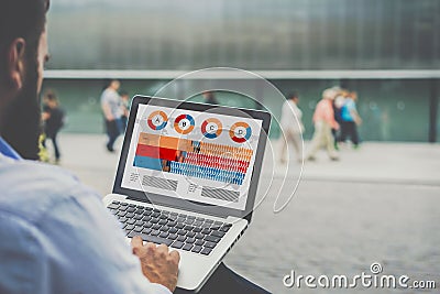 Close-up laptop with graphs, diagrams and charts on screen in hands of businessman sitting outdoors and working. Stock Photo