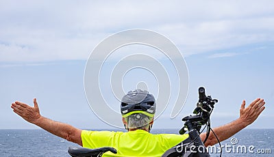 Back view of cyclist man enjoying freedom resting at sea on the cliff after activity with his electro bike Stock Photo
