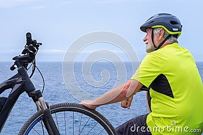 Back view of cyclist man resting at sea on the cliff after activity with his electro bike. Looking away at horizon Stock Photo