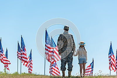 View of father in military uniform holding hands with child near american flags Stock Photo