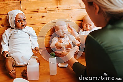 Back view of female doll maker holding caucasian rebeorn while sitting at table in homemade workshop. Stock Photo