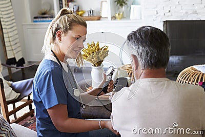 Back view of female healthcare worker measuring the blood pressure of senior man during a home visit Stock Photo