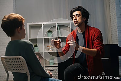 Back view of focused schoolboy sitting on chair listening young music teacher talking and gesturing Stock Photo