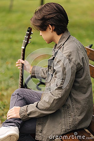 Back view of handsome teenage playing acoustic guitar with capo. Boy sitting on bench and playing music Stock Photo