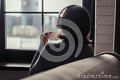 Back view of lonely Ñaucasian young woman enjoying having breakfast with cup of coffee and listenning music in headphones Stock Photo