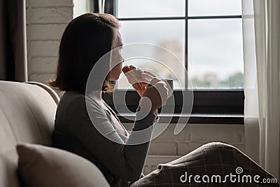 Back view of lonely Ñaucasian young woman enjoying having breakfast with cup of hot chocolate and croissant sitting near window Stock Photo