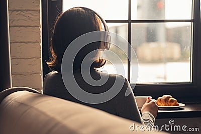 Back view of lonely Ñaucasian young woman enjoying having breakfast with cup of hot coffee, cappuccino and croissant Stock Photo