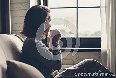 Back view of lonely Ñaucasian young woman enjoying having breakfast with cup of hot coffee and sitting near window at morning. Stock Photo