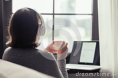 Back view of lonely woman enjoying having breakfast with cup of coffee working on laptop sitting near window in cafe at morning. Stock Photo