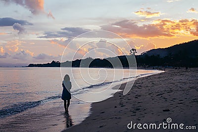 Back view of lonely woman walking on beach in sunset Stock Photo