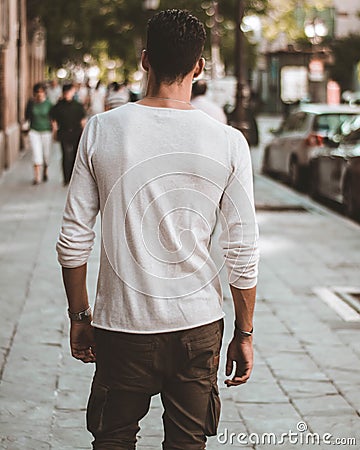 Back view of a male with a white long sleeve t-shirt walking on the sidewalk Editorial Stock Photo