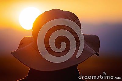 Back view of a man with explorer hat watching scenic sunset. Concept for travel exploration and discovery. Stock Photo