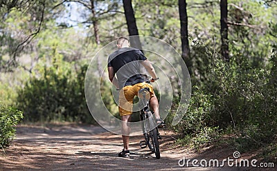 Back view of man sitting on bicycle on forest road Stock Photo