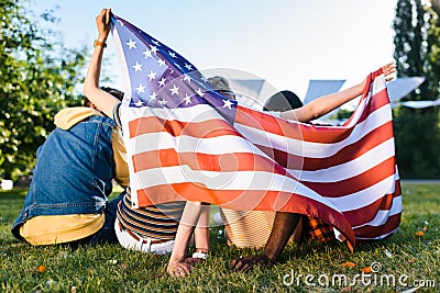 back view of multiracial friends with american flag sitting on green grass Stock Photo