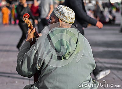 Back view of an old man with traditional dress and designer round cap sitting on road playing a musical instrument Sitar, Canada Editorial Stock Photo