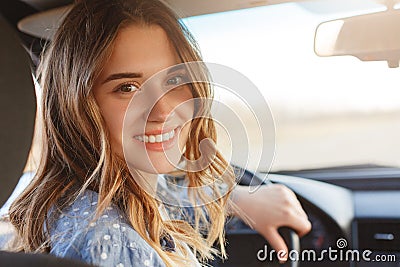 Back view of pretty smiling woman with broad smile, has attractive look, sits at wheel in car, has break after long trip, looks di Stock Photo