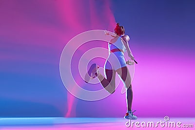 Back view. Professional female athlete running away isolated on blue studio background in mixed pink neon light. Healthy Stock Photo