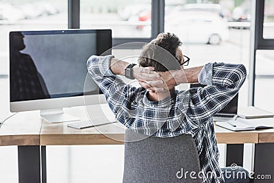 back view of programmer sitting with hands behind head Stock Photo