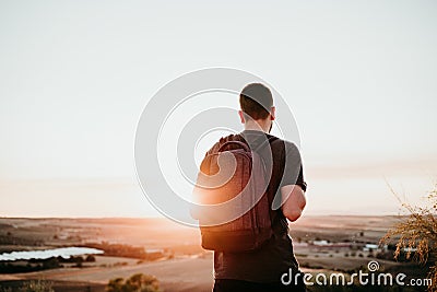 Back view of relaxed hiker man with backpack at sunset in mountain. Hiking and nature Stock Photo