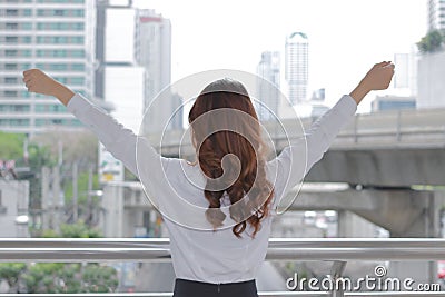 Back view of successful young Aian business woman raising her hands at urban building city background. Stock Photo