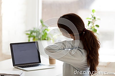 Back view of tired woman touching neck at work desk Stock Photo