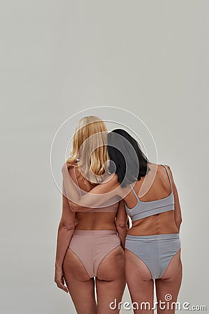 Back view of two mature caucasian women in underwear standing together while posing over light background Stock Photo