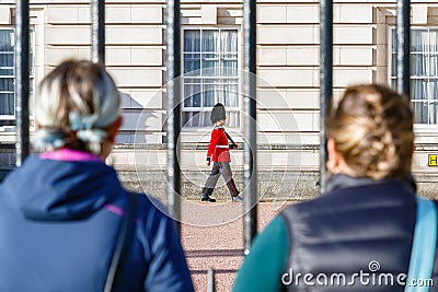 Back view of two tourists watching a sentry of Grenadier Guards patrolling outside Buckingham Palace Editorial Stock Photo