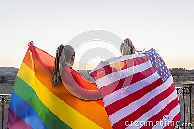 Back view unrecognizable lesbians couple holding lgtb rainbow flag and American flag at sunset.United States and gay pride flags Stock Photo
