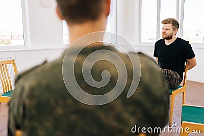 Back view of unrecognizable psychologist talking to group of male veterans in camouflage uniform sitting in circle Stock Photo