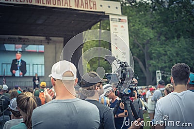 Back view video operator wear cap operating camcorder at live Memorial March event in Dallas Editorial Stock Photo