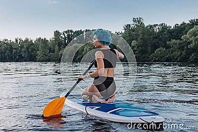 back view of woman with blue hair sitting on paddle board Stock Photo