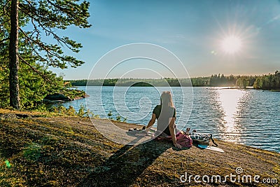 Back view of woman relaxing and enjoys warm evening Sunset on flat stone slope close to river. Scandinavian nature landscape, Stock Photo