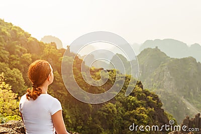 Back view woman tourist looking far away and enjoying valley and hills view from top of a mountain Stock Photo