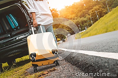 Back view of yellow suitcase dragging baggage suitcase alone road trip for loading into SUV car. People lifestyles and vacation Stock Photo