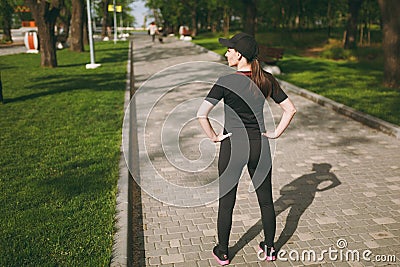 Back view Young athletic beautiful brunette girl in black uniform, cap standing, resting and looking aside before or Stock Photo
