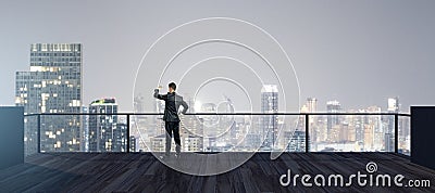 Back view of young businessman looking into the distance on rooftop with night sky and wide city view. Success, future and vision Stock Photo