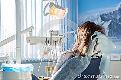Back view of young female patient visiting dentist office sitting at dental chair. Clinic stomatology Stock Photo