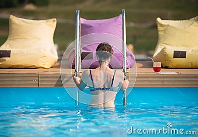 Back view young female in swimsuit coming out from the water of a swimming pool at the resort Stock Photo