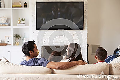 Back view of young Hispanic family of four sitting on the sofa watching TV, mum looking at dad Stock Photo