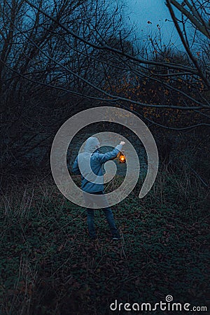 Back view of a young male with a lantern standing in front of a river on a spooky, scary evening Stock Photo
