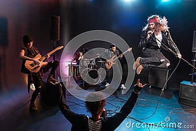 Back view of young woman gesturing rock and roll hand sign and looking at band Stock Photo